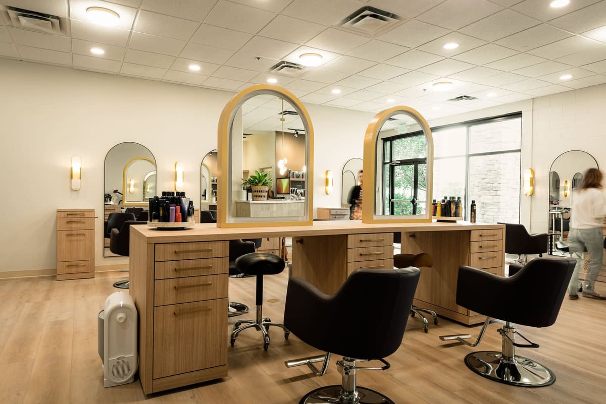 Salon floor with double-sided oak styling islands, arched brass-framed mirrors and black chairs