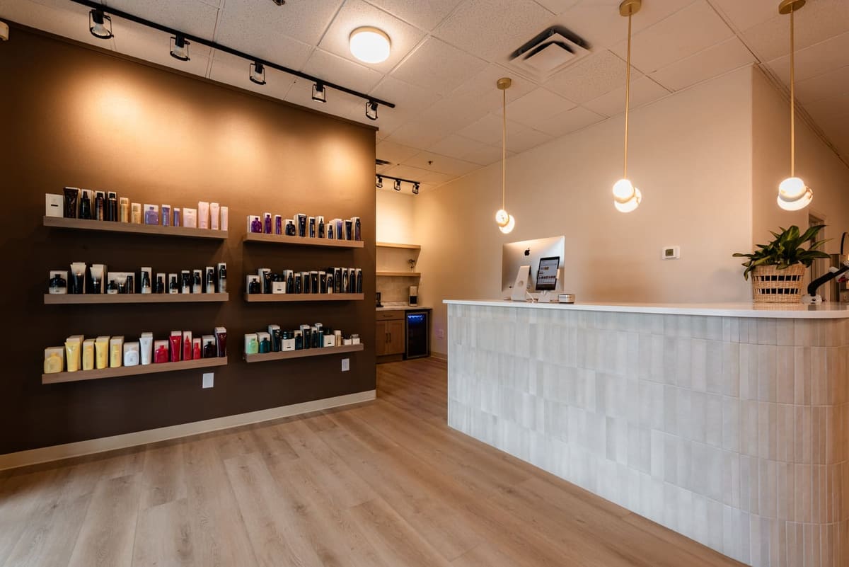 Reception desk in pale stacked tile facing a dark retail wall of lit product shelves