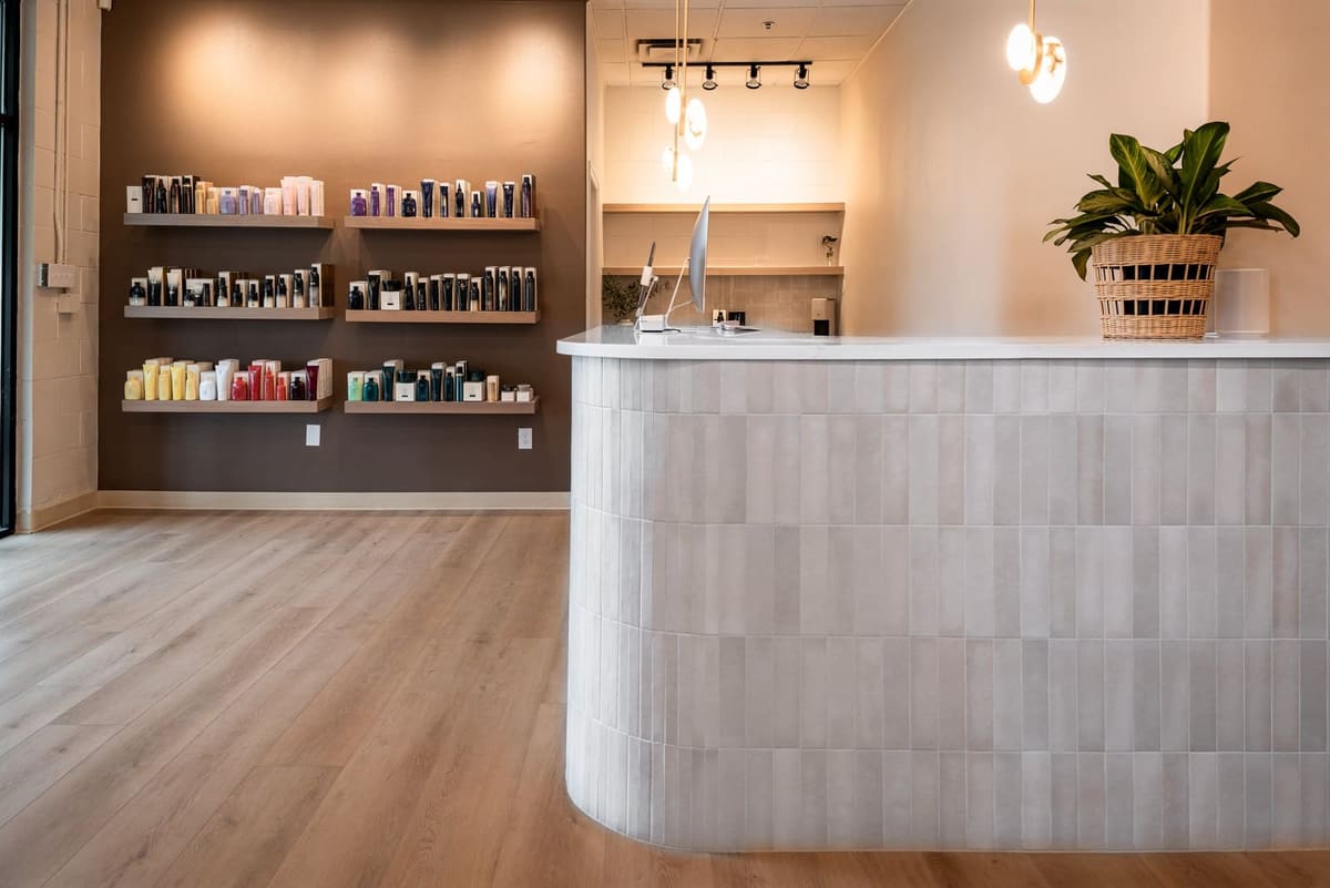 Curved reception desk in pale stacked tile beside dark retail shelving under warm track lights