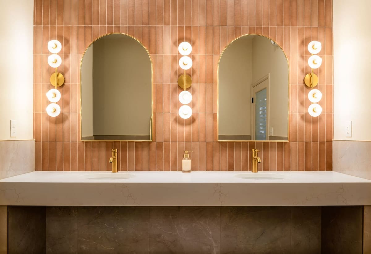 Shampoo vanity wall in vertical terracotta tile with arched mirrors, globe sconces and brass faucets