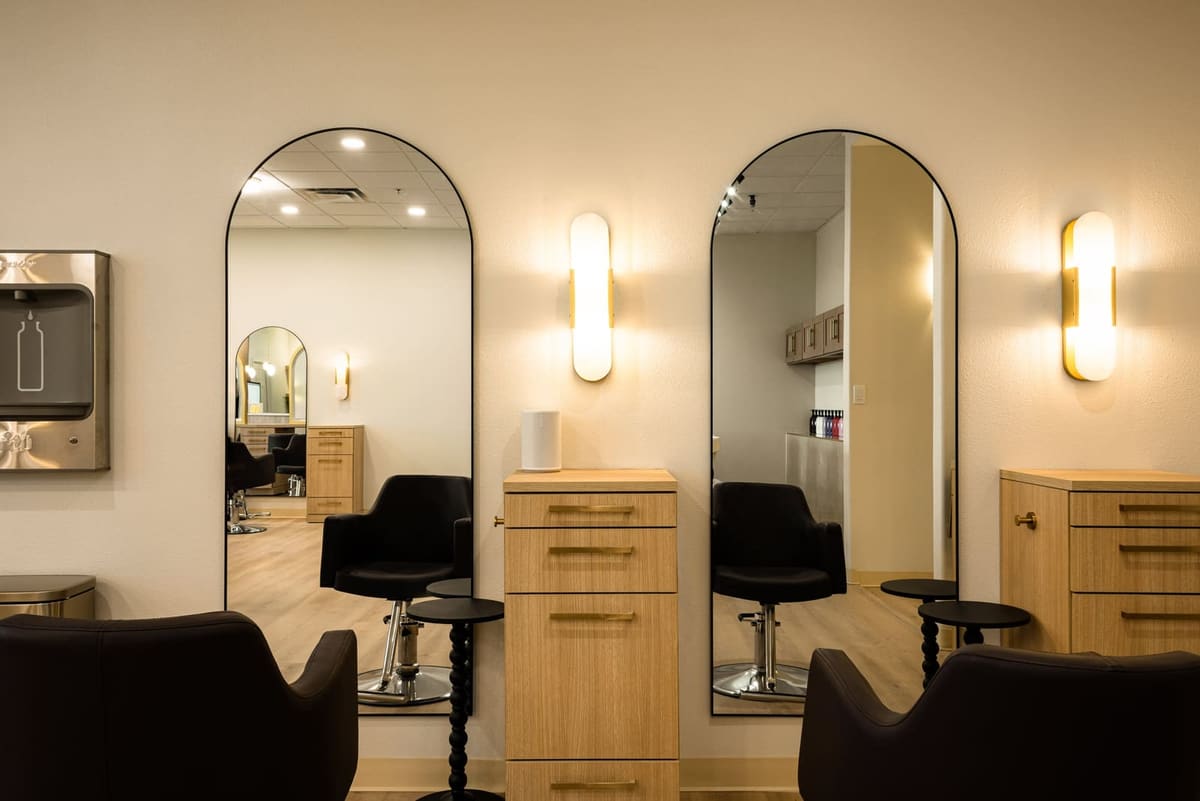 Tall arched black mirrors with brass sconces over light oak styling stations