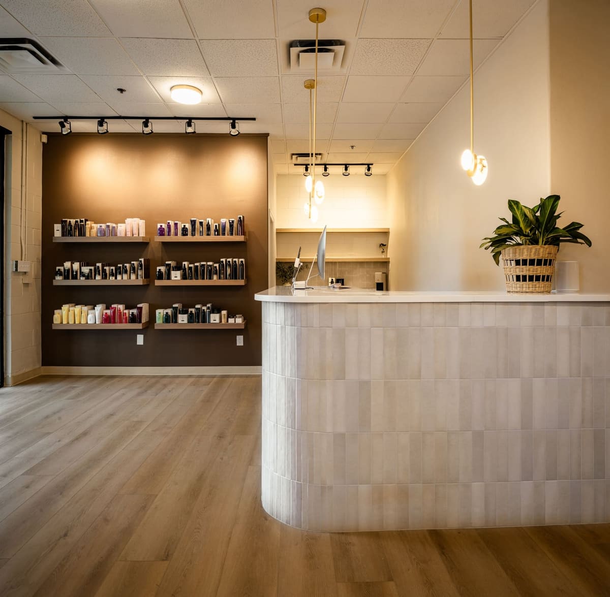 Salon reception desk in pale stacked tile with a glass pendant and lit retail shelves behind
