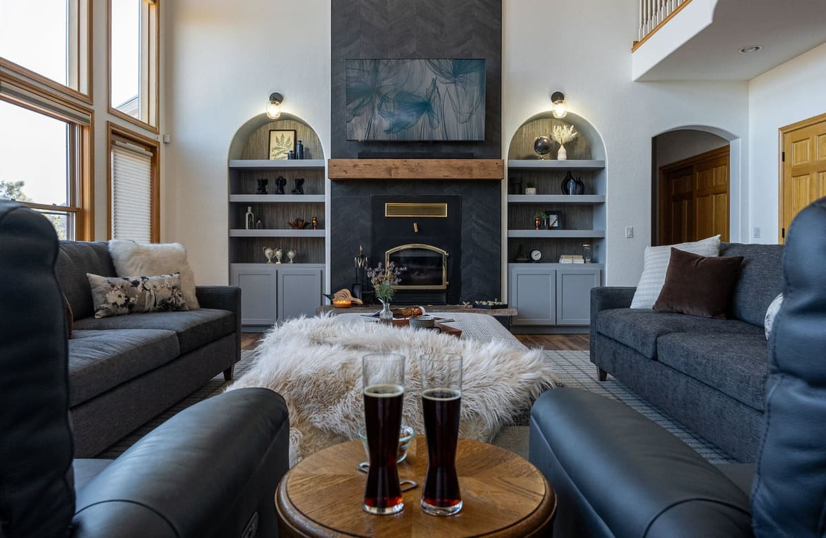 Living room facing a charcoal chevron fireplace with a beam mantel, wood stove and lit arched built-in niches