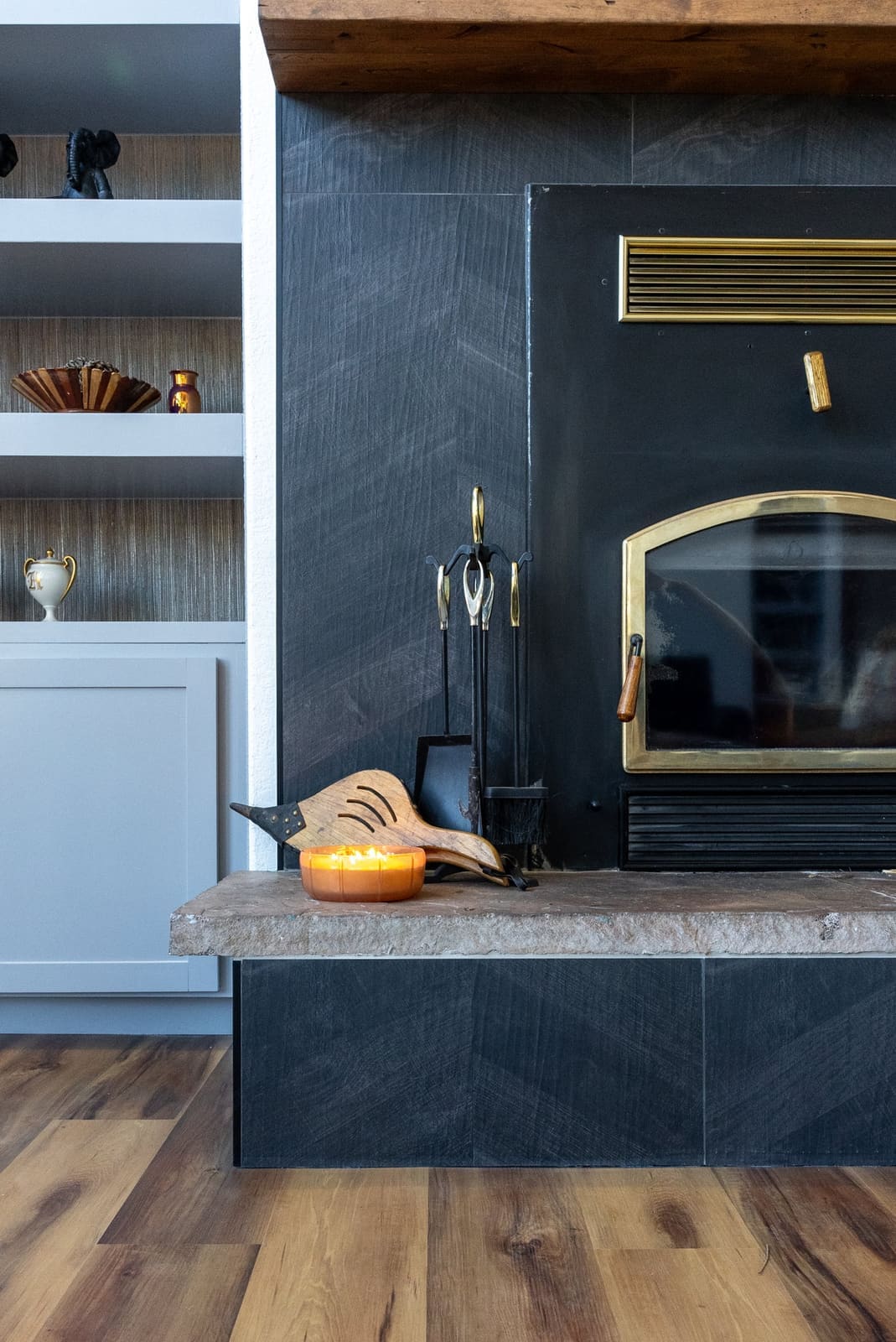 Fireplace detail with charcoal chevron tile, a brass-trimmed wood stove, raw stone hearth and brass fire tools