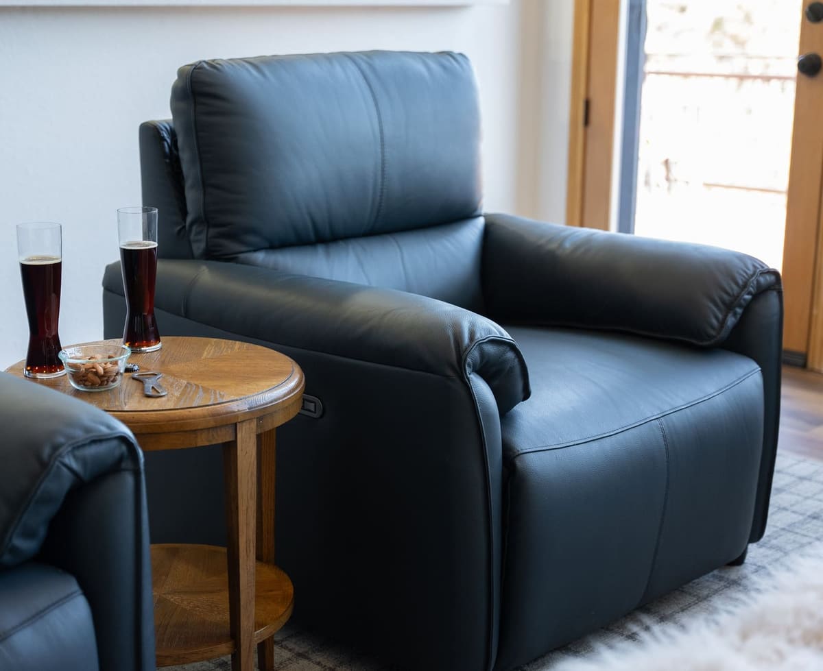 Navy leather power recliner beside a round oak side table with drinks, set against a plaid area rug
