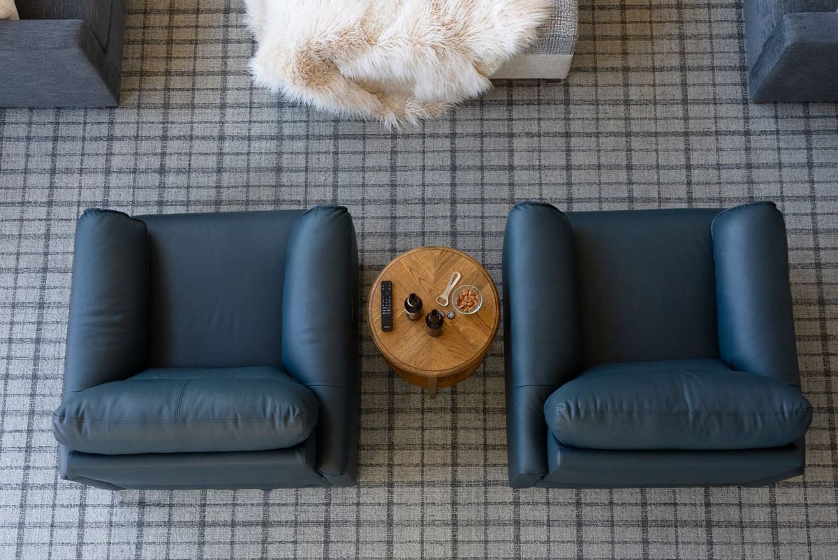 Two navy leather chairs flanking a round oak side table set with drinks and almonds on a plaid rug