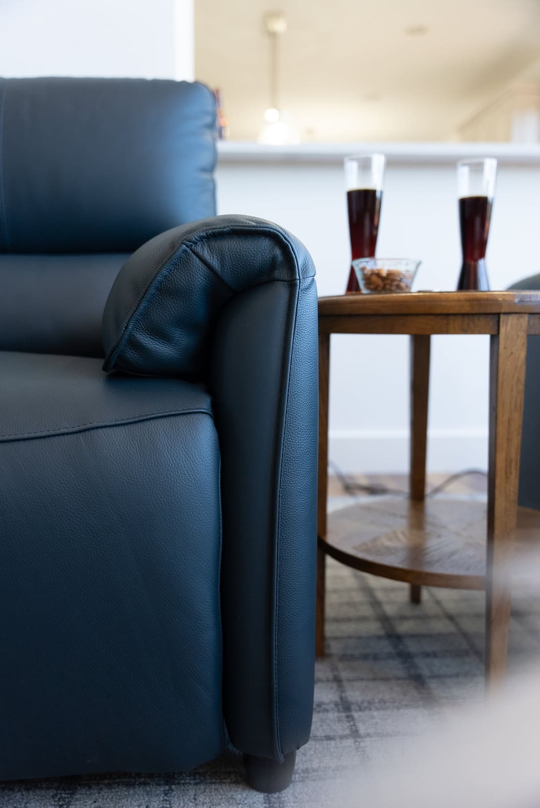 Close view of a navy leather recliner arm and round wood side table holding two glasses and a bowl of almonds