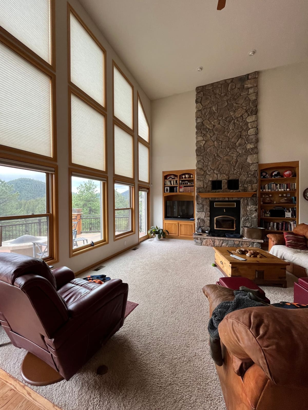 Before the remodel: stone fireplace and oak shelving beside tall windows, with a leather recliner in front