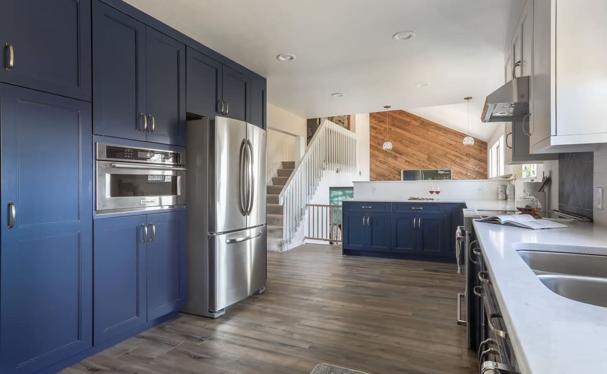 Navy floor-to-ceiling cabinets framing a stainless fridge and wall oven, with a wood-plank accent wall beyond
