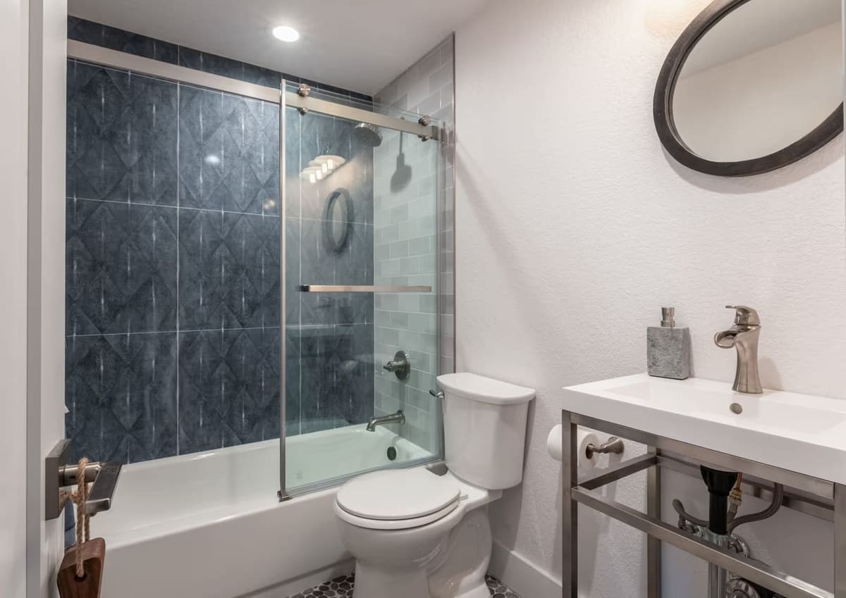 Bathroom with navy diamond-pattern tub surround, sliding glass shower door, and steel console sink