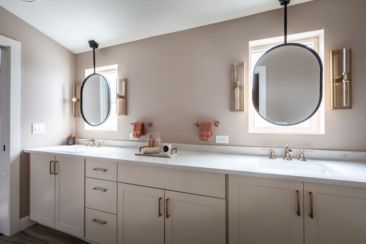 Double vanity with two ceiling-hung oval mirrors over windows, champagne bronze sconces and rust towels