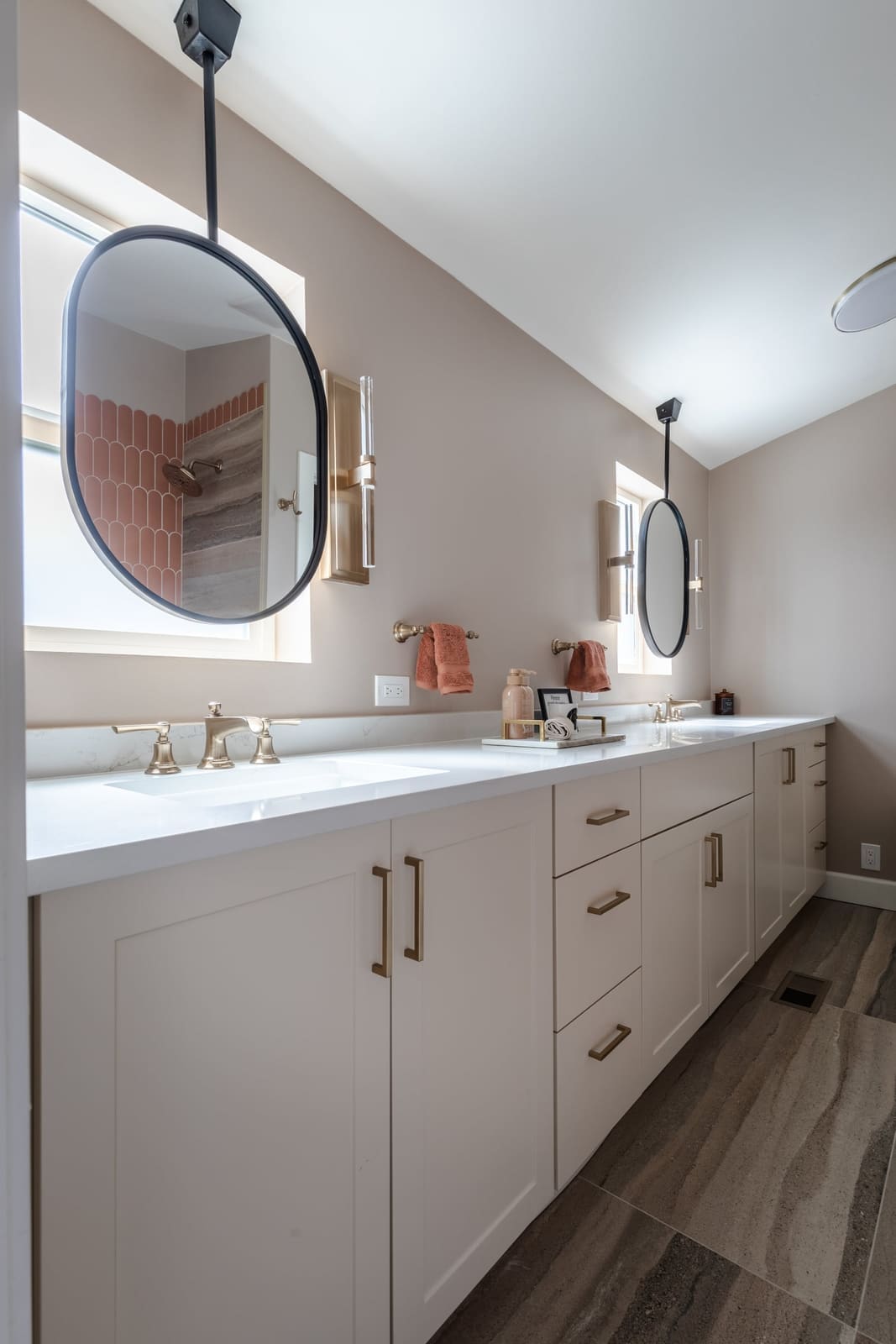 Bathroom double vanity in cream shaker cabinetry with ceiling-hung black oval mirrors set in front of windows