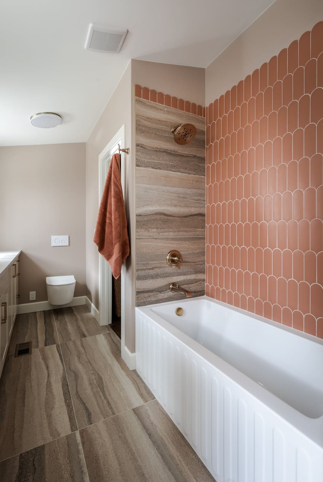 Tub and shower wall with terracotta fan tile, a striated porcelain panel and champagne bronze shower trim