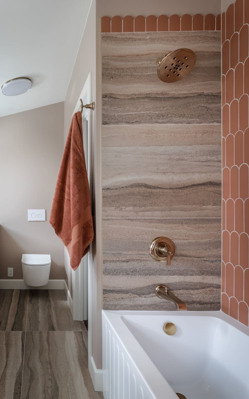 Close view of a striated porcelain shower panel with champagne bronze trim and a scalloped terracotta tile edge