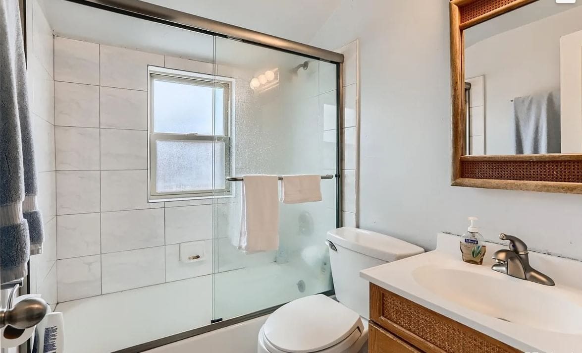Before the remodel: bathroom with a sliding glass tub door, white wall tile and a basic vanity