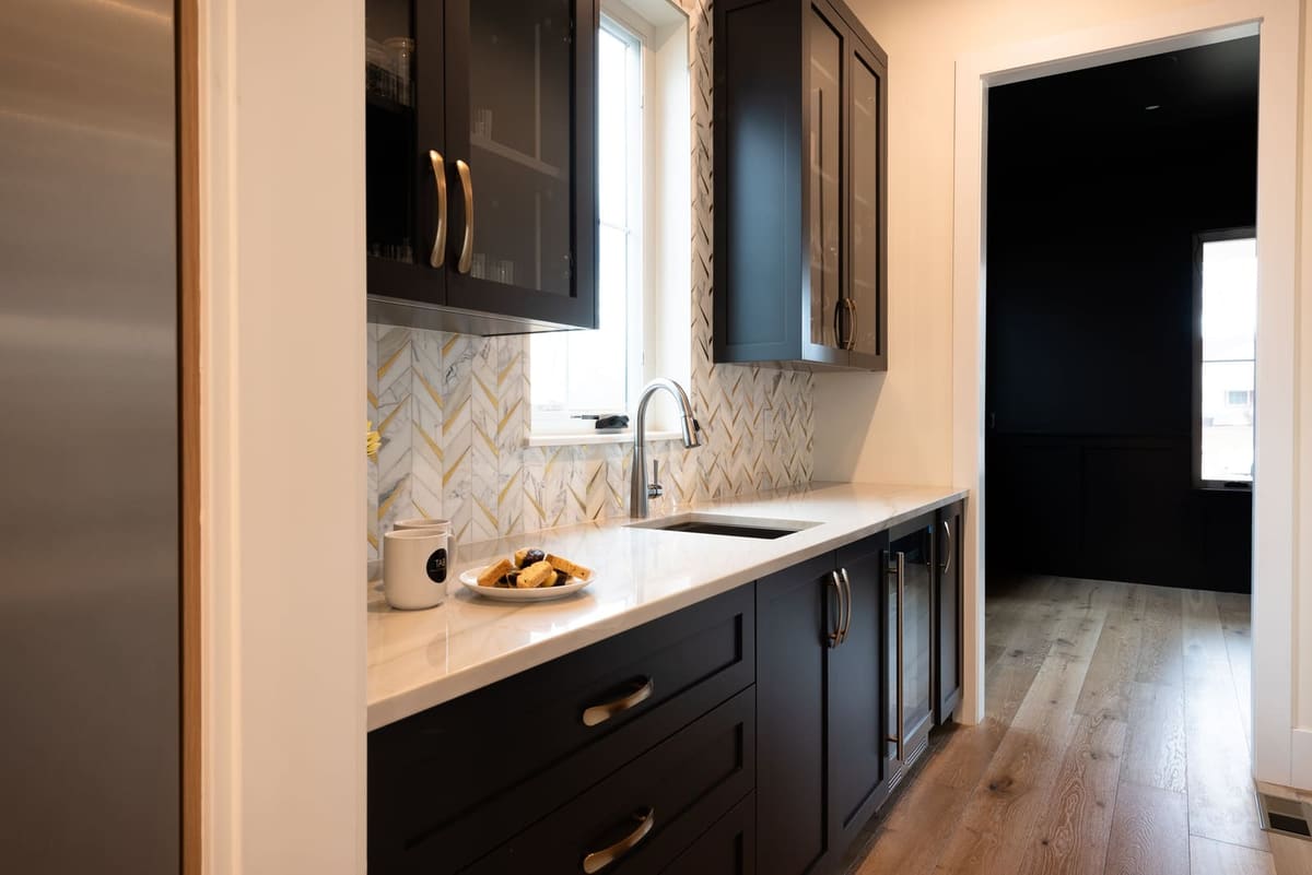 Butler's pantry with black shaker cabinetry, quartzite counters, a beverage fridge and chevron tile to the ceiling