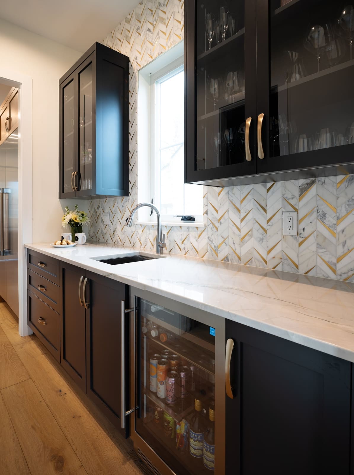 Butler's pantry with black glass-front uppers holding stemware, a beverage fridge and quartzite counters