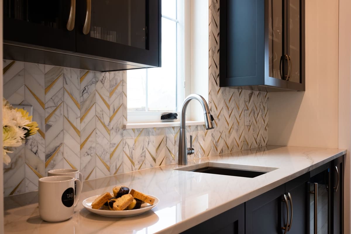 Marble chevron backsplash with brass inlay behind a stainless pull-down faucet and undermount sink