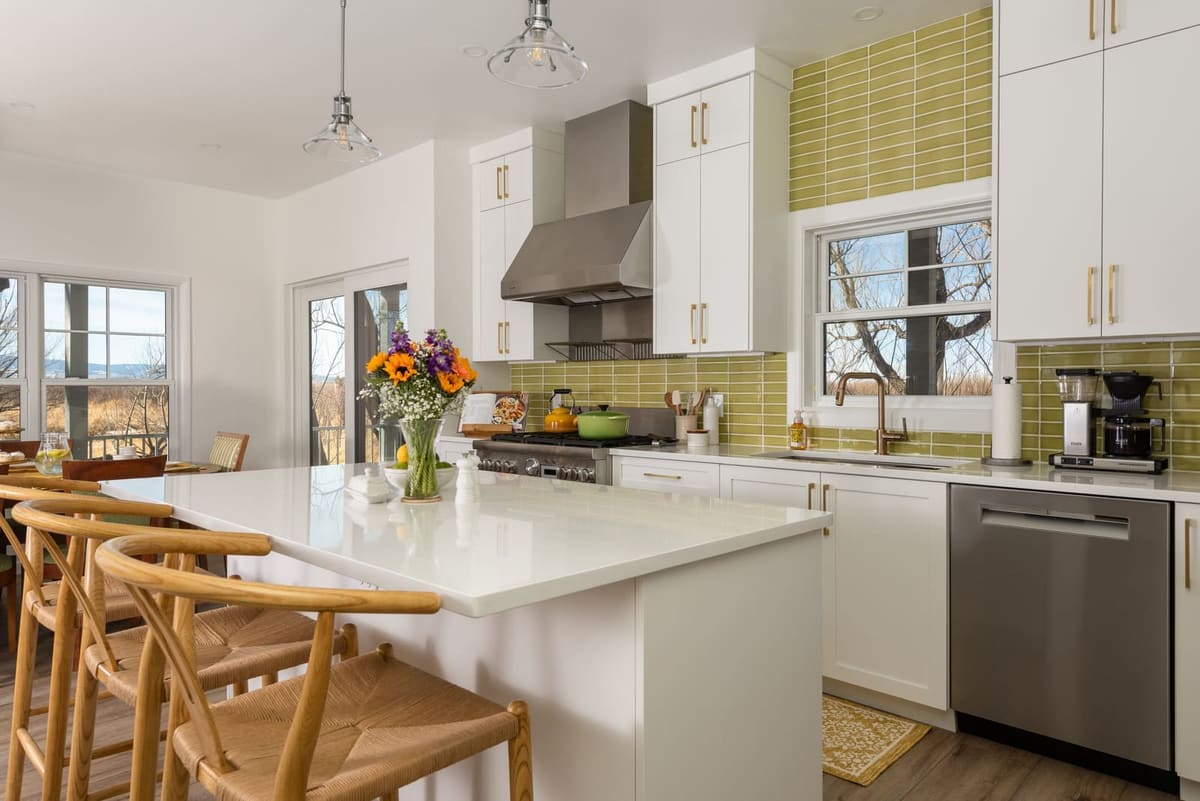 White kitchen with chartreuse stacked tile, brass pulls, a stainless range hood and wishbone counter stools
