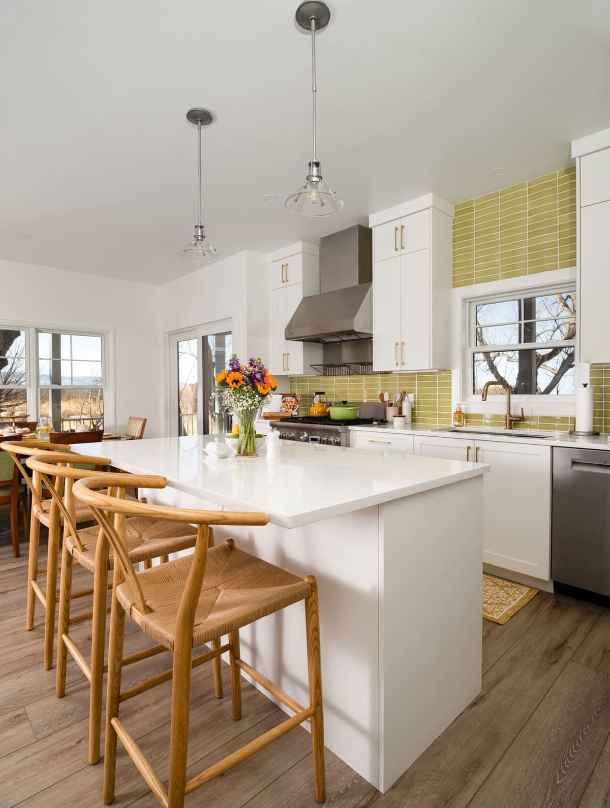 Kitchen island with woven rush counter stools, white cabinets, chartreuse stacked tile and a stainless hood