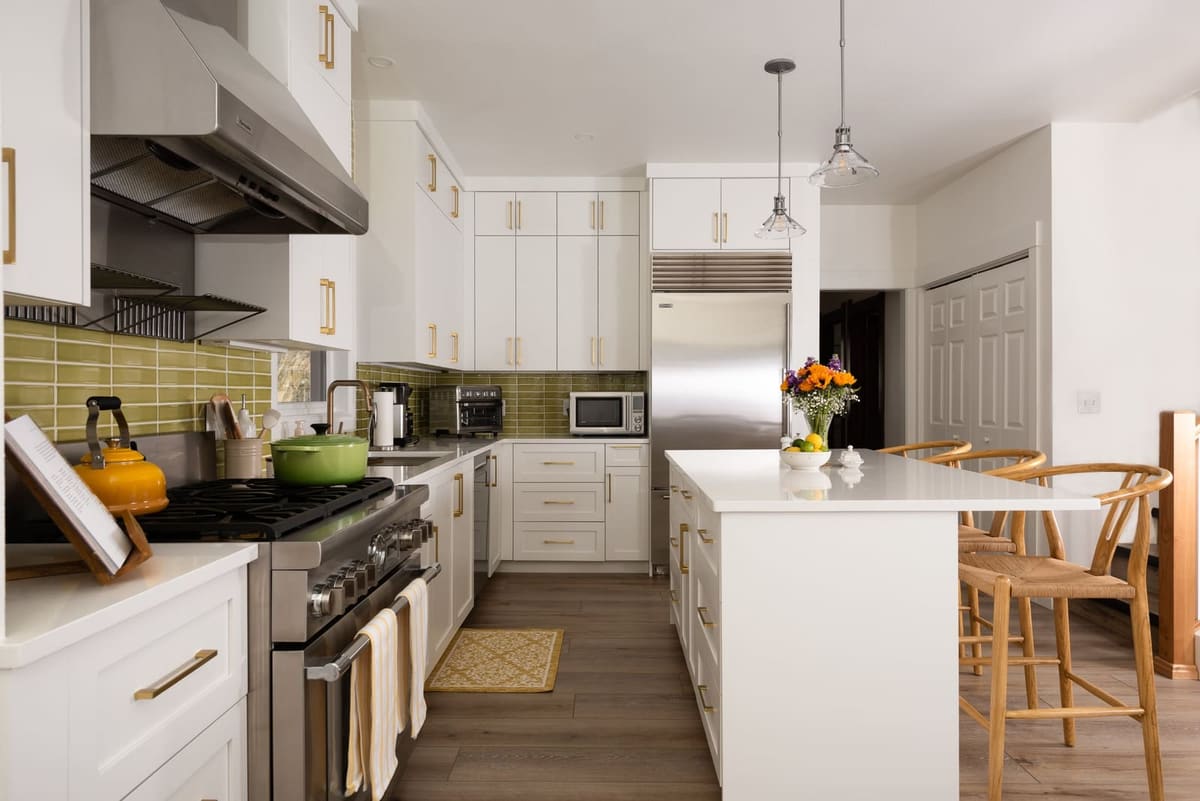 Galley view of a white kitchen with brass pulls, chartreuse tile, a pro range and a stainless refrigerator