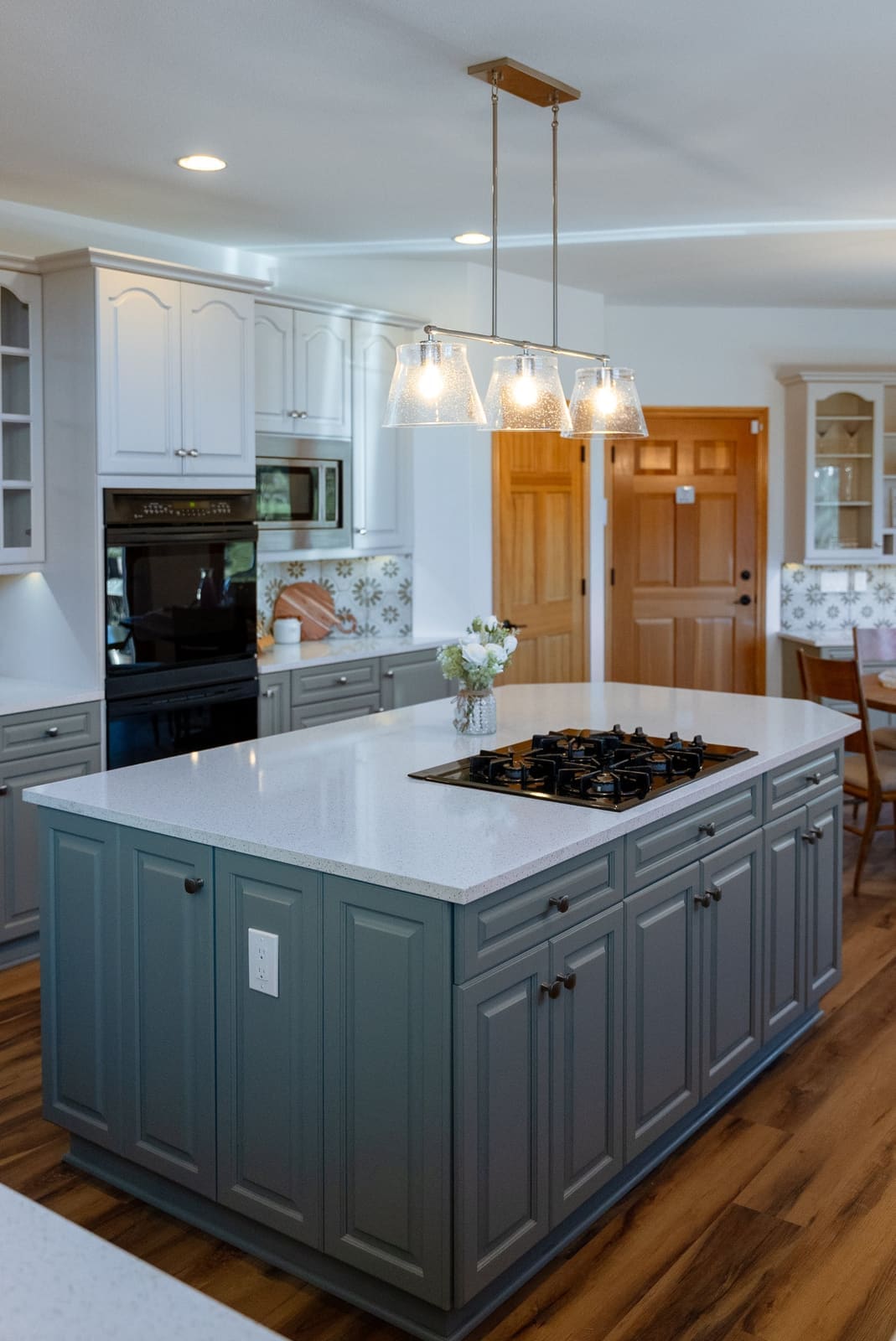 Kitchen island in slate blue raised-panel cabinetry with a gas cooktop, white quartz top and seeded glass pendant