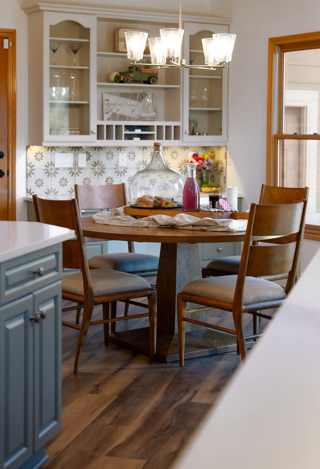 Breakfast nook with a round wood pedestal table, seeded glass chandelier and built-in glass-front hutch