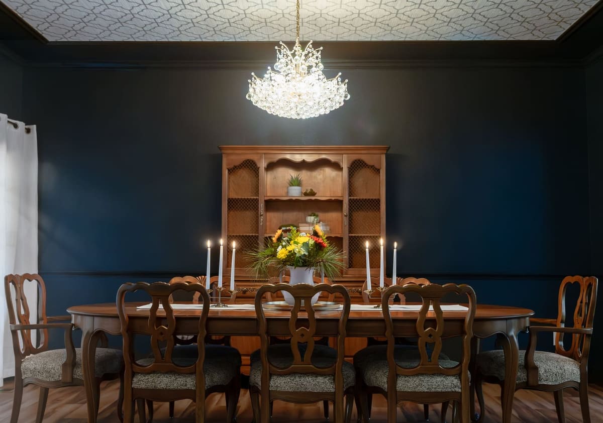 Dining room with navy walls, a geometric wallpapered tray ceiling, crystal chandelier and French provincial chairs