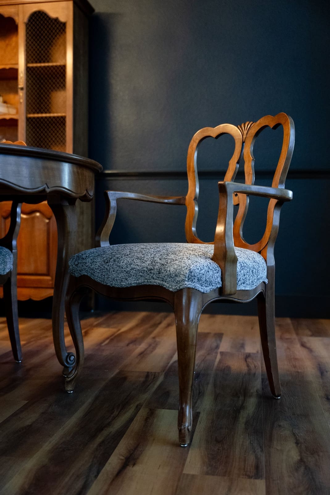 French provincial dining armchair reupholstered in gray tweed against a navy wall and a mesh-front hutch