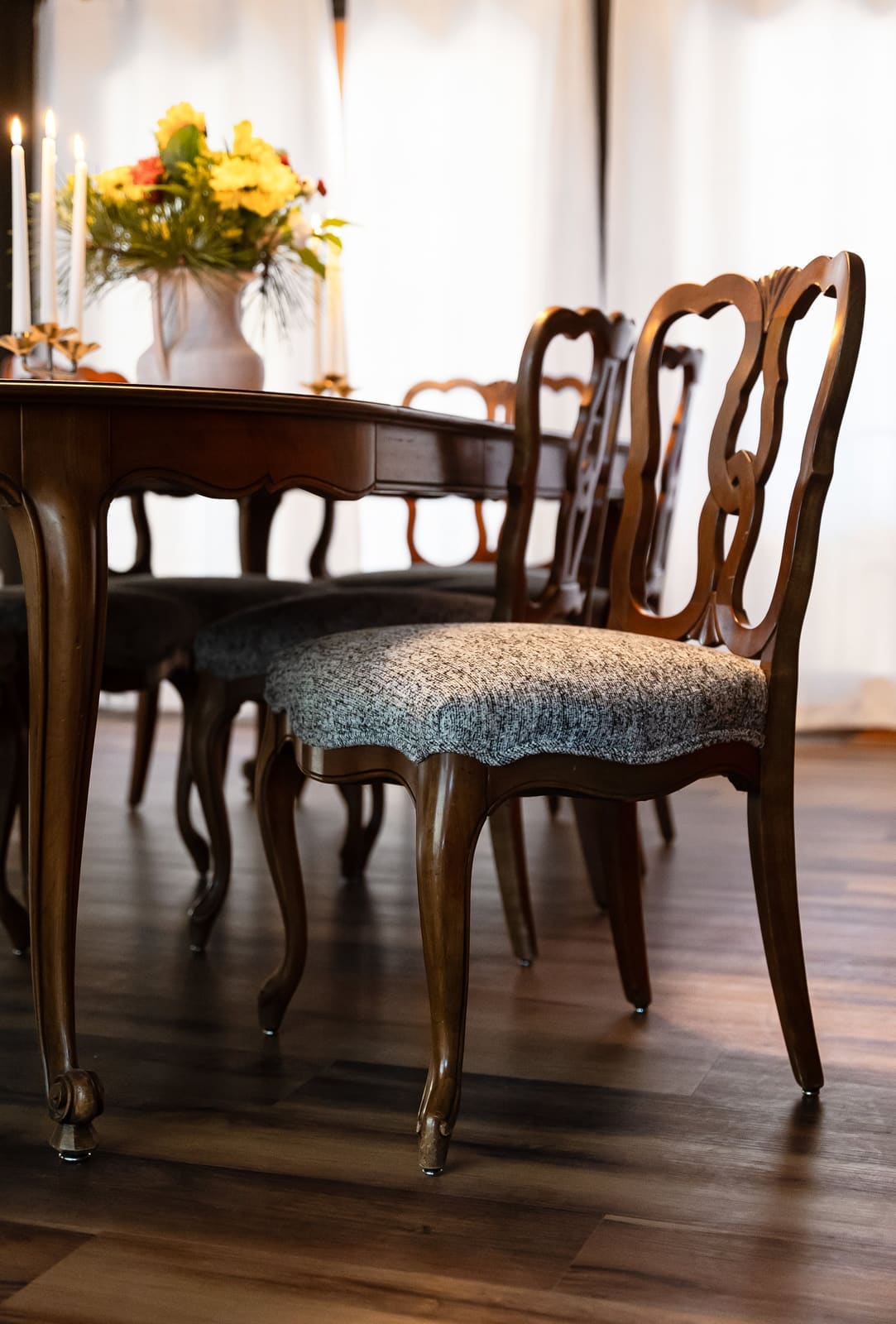 Detail of a carved French provincial dining chair with a gray tweed seat beside a navy dining room wall