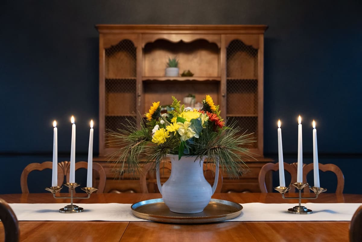 Dining table centerpiece with brass candelabras in front of a painted hutch against a navy dining room wall