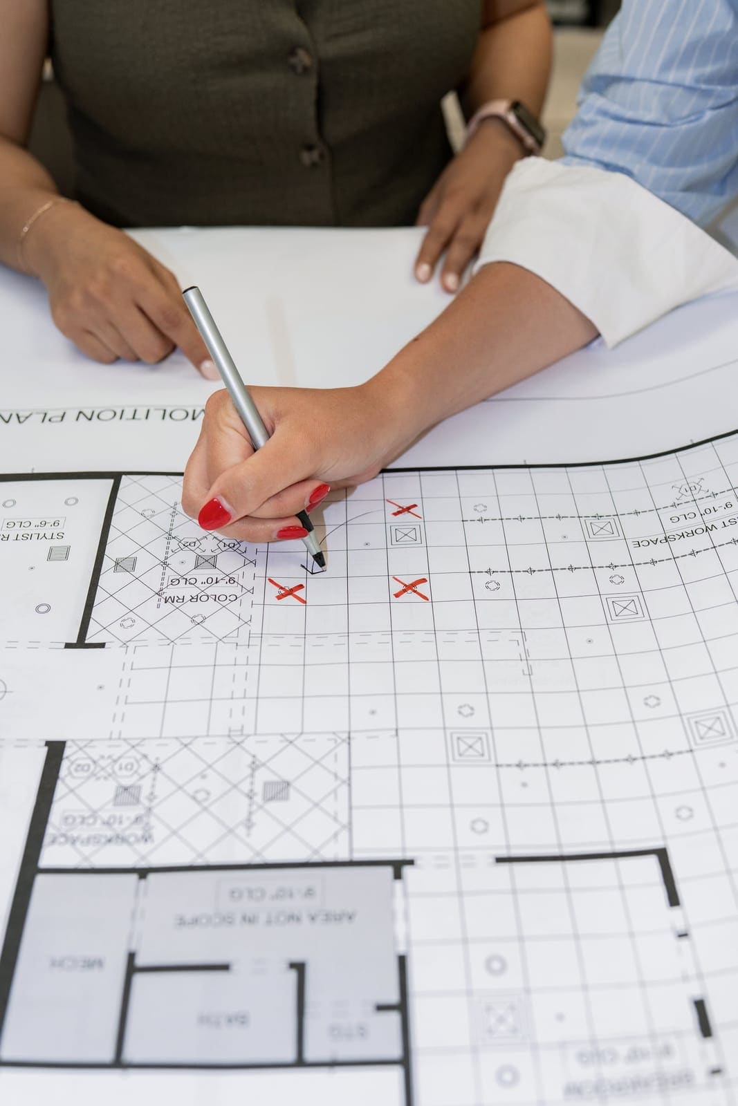 Hands marking up a printed construction floor plan with red pens at the TAB studio table