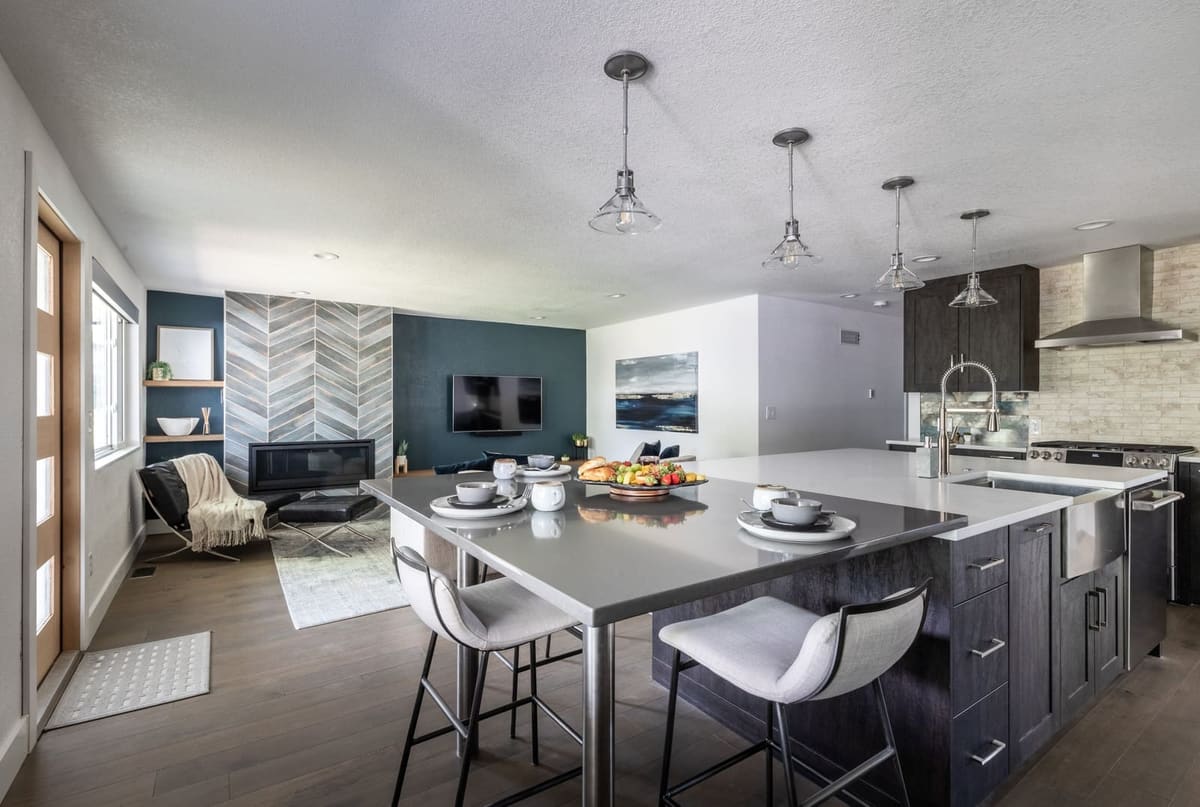 Open kitchen with a charcoal-stained island and white bar stools, a chevron tile fireplace beyond