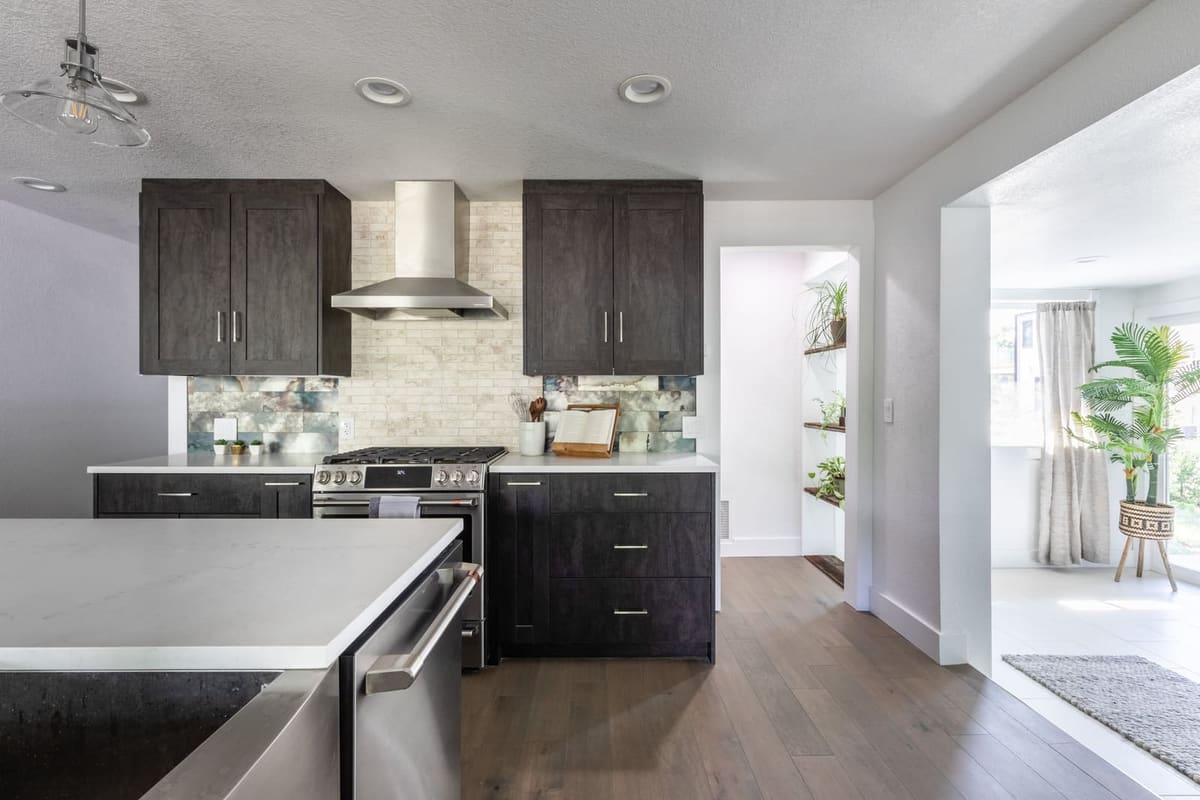 Charcoal-stained cabinets around a stainless range hood and a stacked stone mosaic backsplash