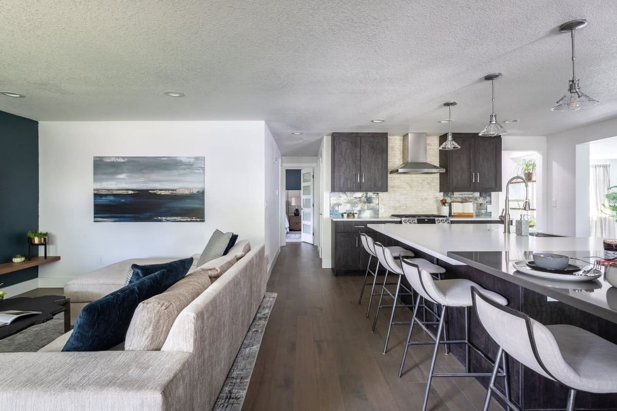 View from the living room sofa to the charcoal kitchen island and white bar stools