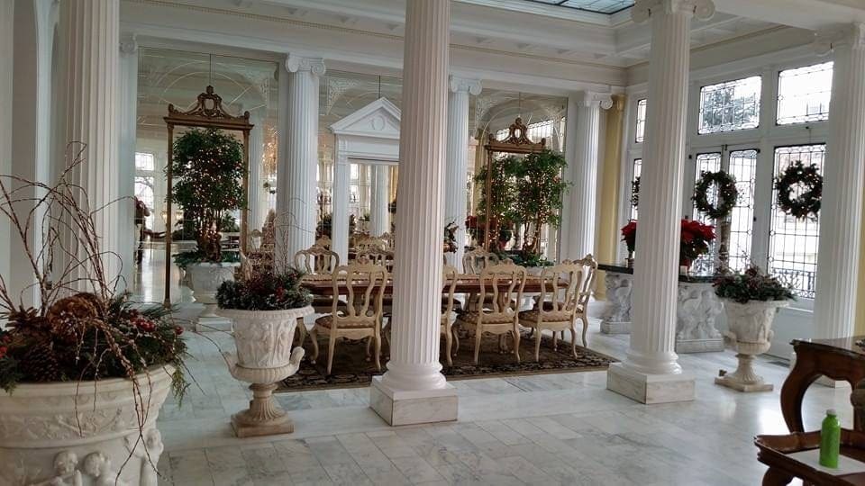 White-columned conservatory dressed with wreaths, garland and poinsettia urns around a set dining table
