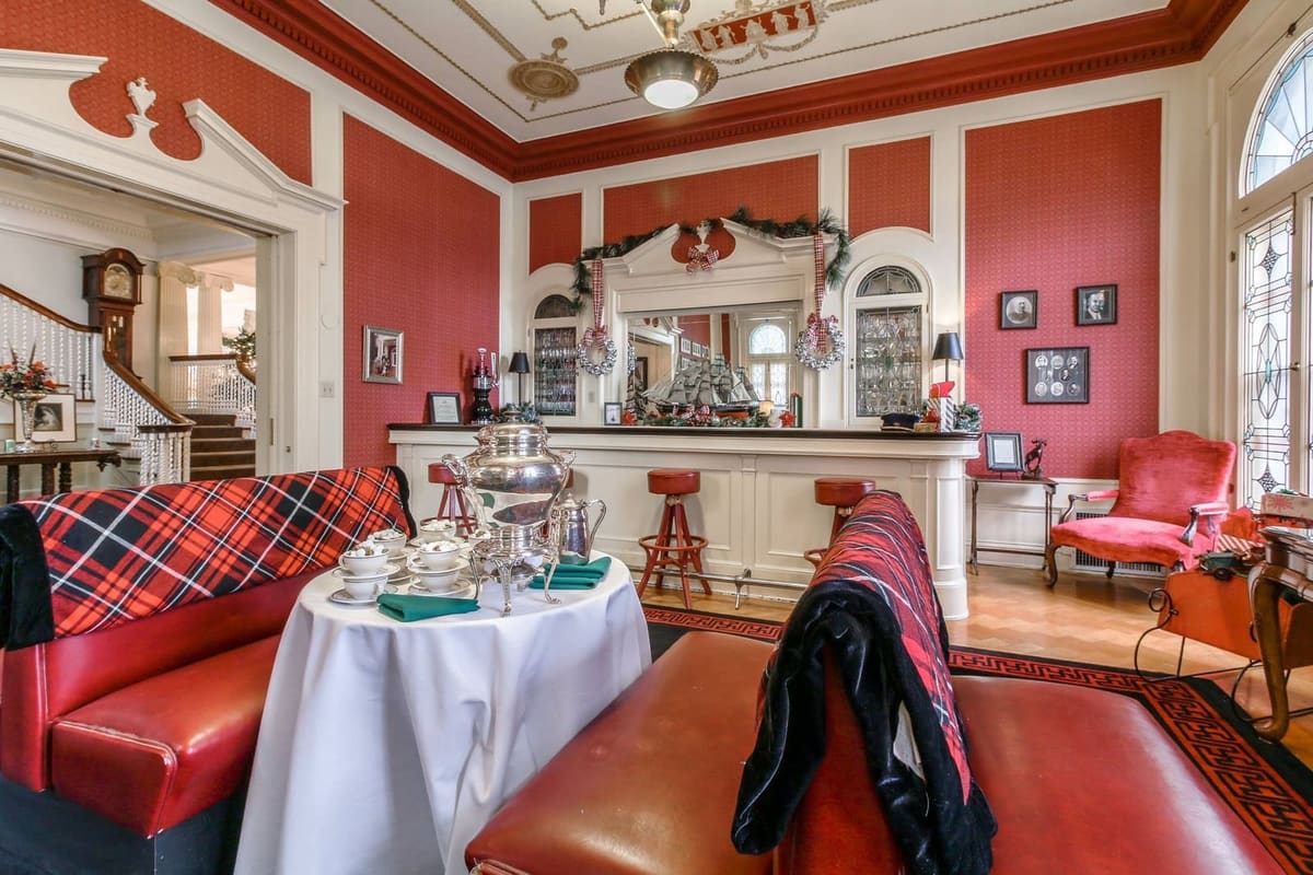 Holiday reception room set with plaid-draped seating, a cocoa table and a red and cream bar beyond