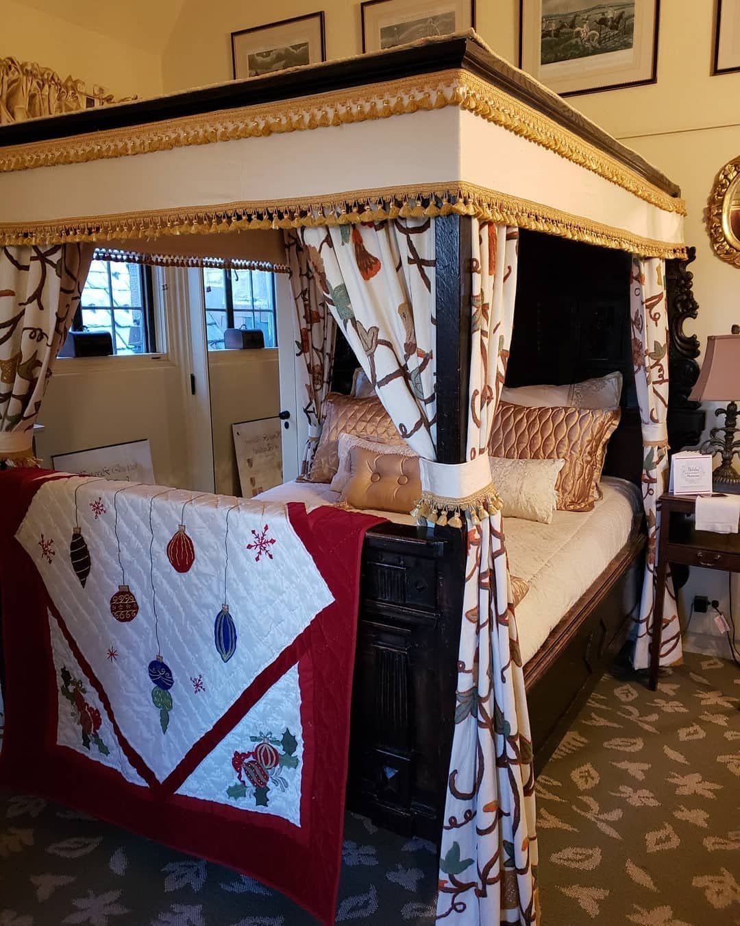 Canopy bed with a white Christmas quilt appliquéd with ornaments, draped in red