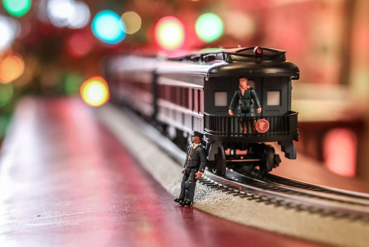 Model passenger train with a conductor figure on a red table under soft colored tree lights