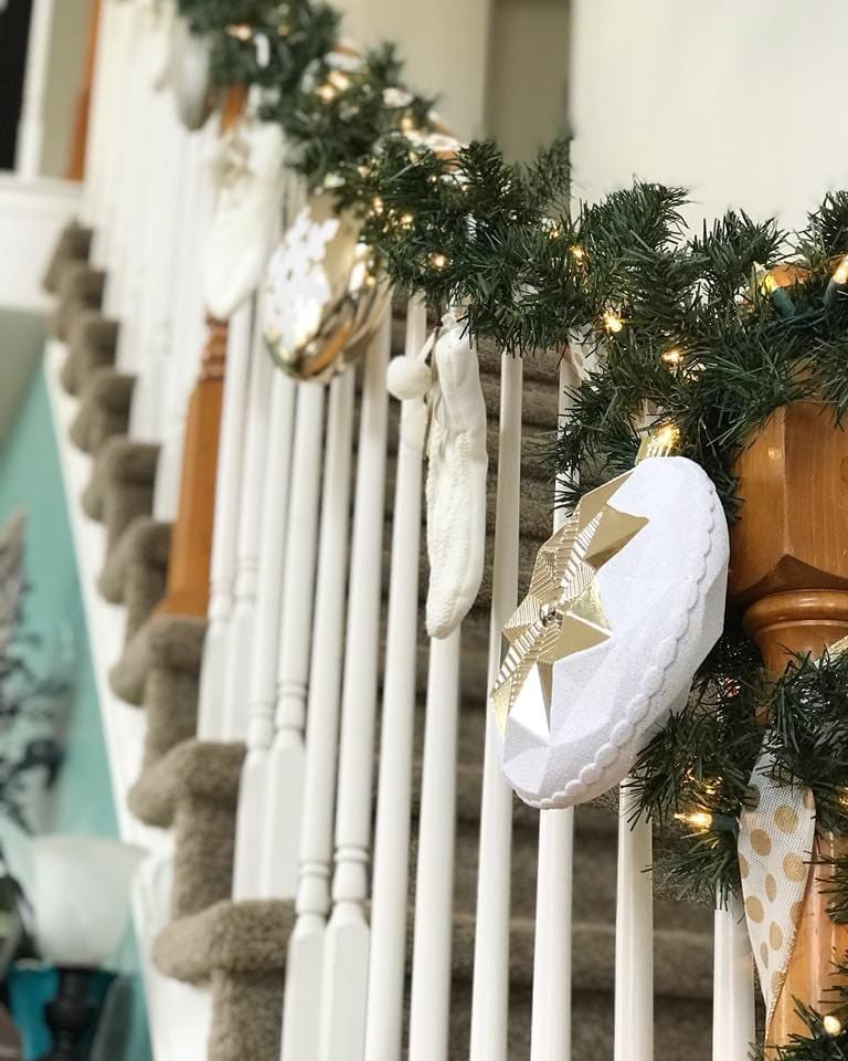 Lit garland wrapped along a white stair rail with cream and gold star ornaments