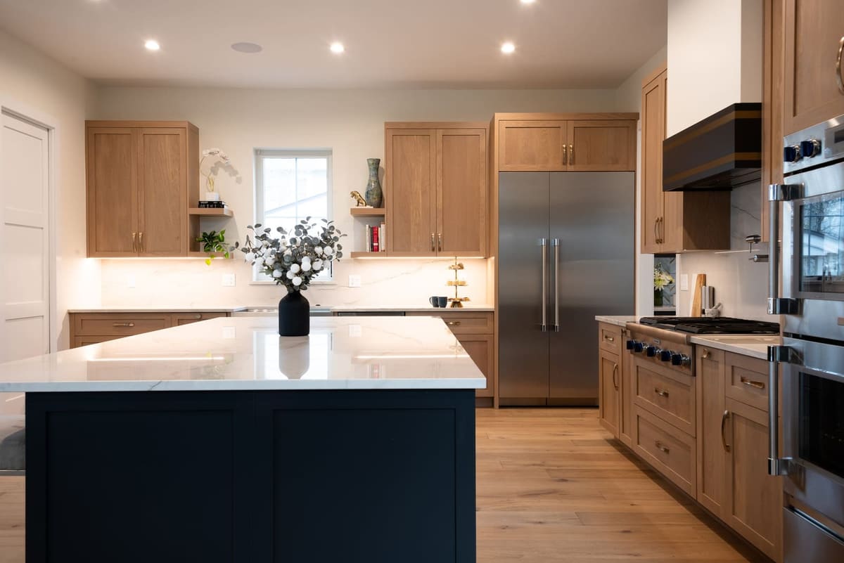 Navy island with a white quartz top in a white oak kitchen with a stainless built-in refrigerator