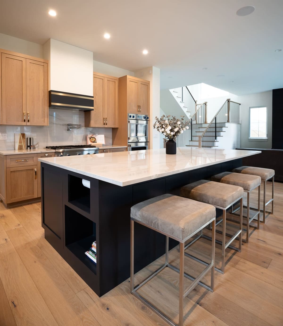 Navy island with open end shelving and upholstered stools, a modern stair beyond