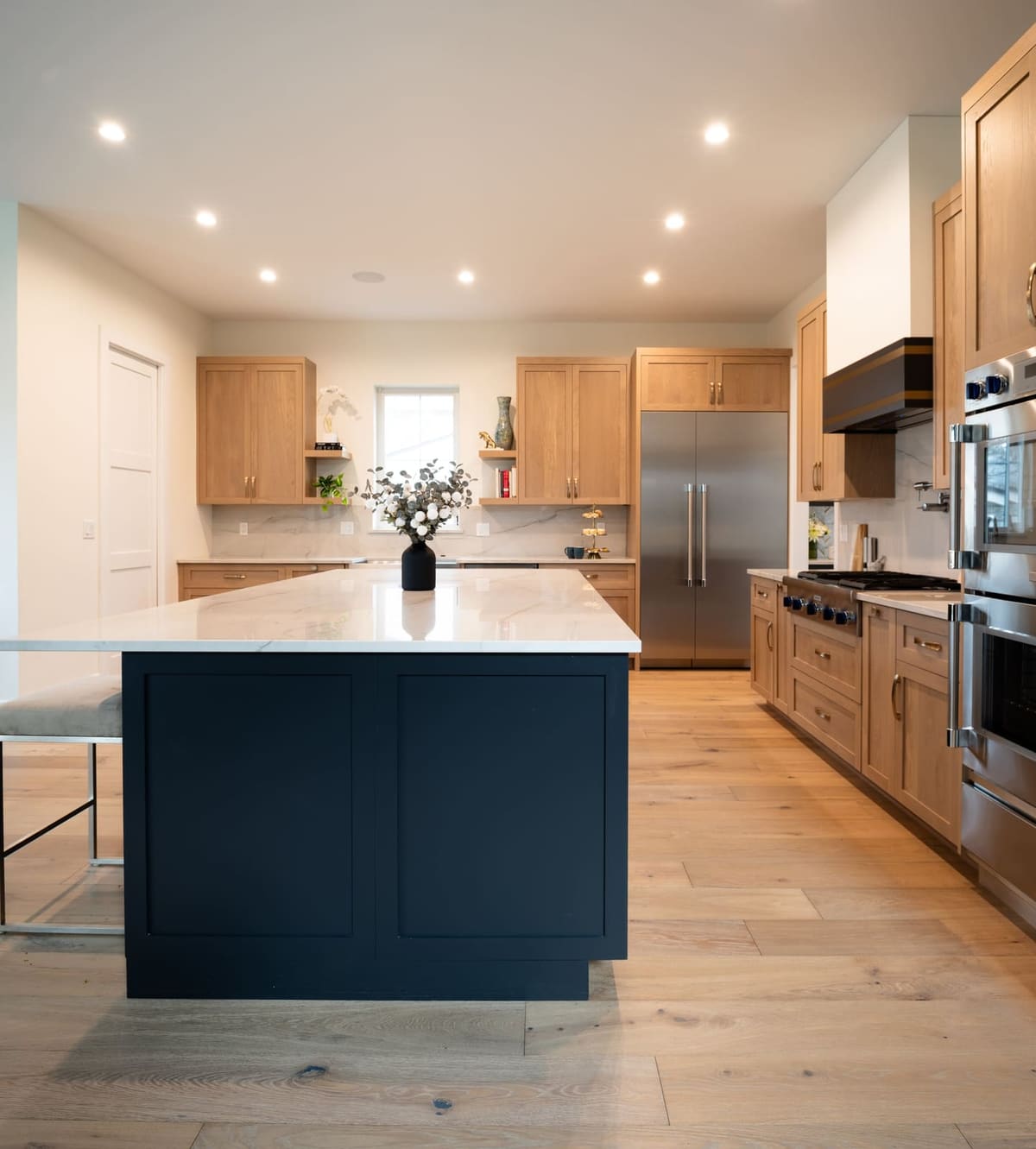 Navy kitchen island centered in a white oak kitchen with stainless appliances