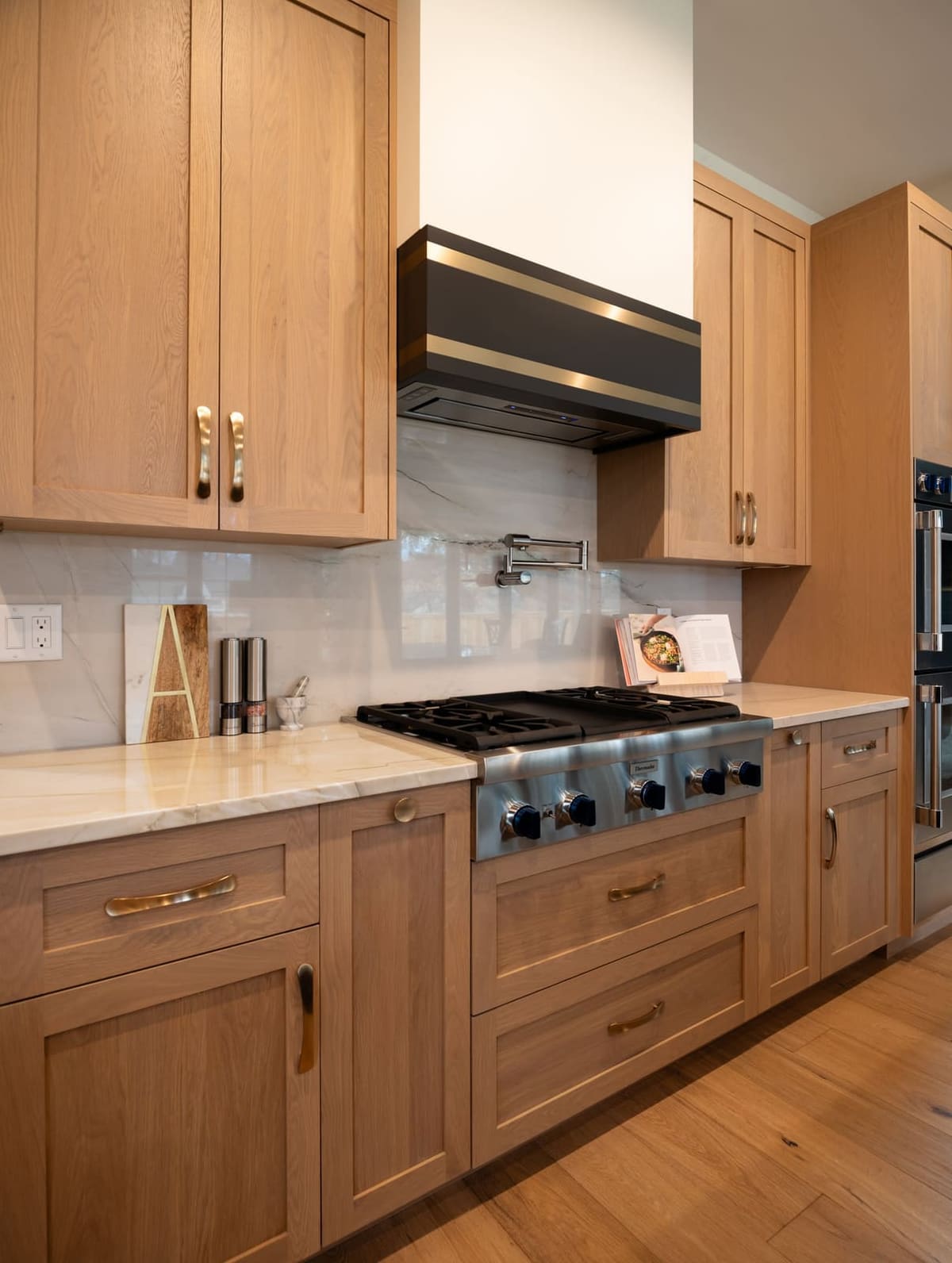 White oak cabinets around a pro range top with a black hood liner and white tile backsplash