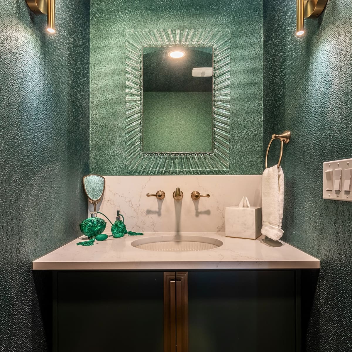 Emerald powder room vanity with a wall-mounted brass faucet, white stone counter and brass sconces