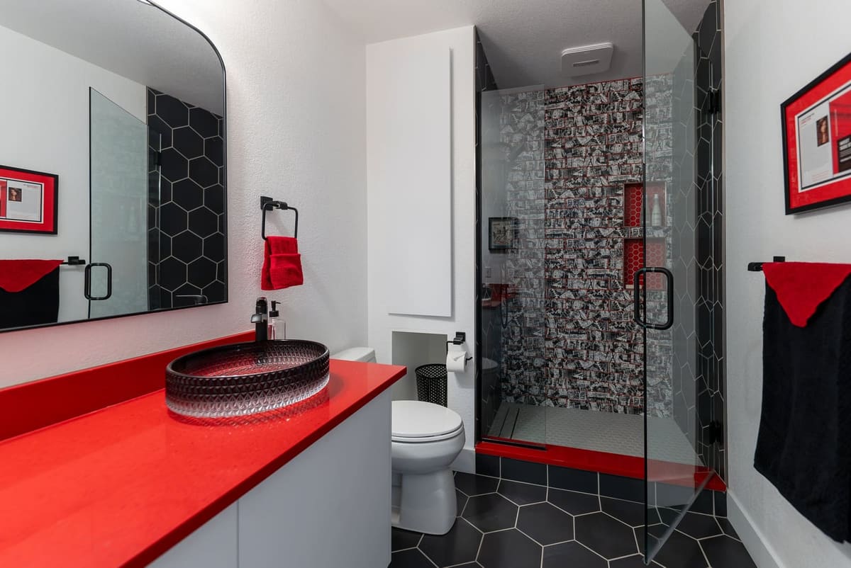 Bathroom view of a red quartz vanity and black fixtures beside a glass shower clad in graffiti-print tile