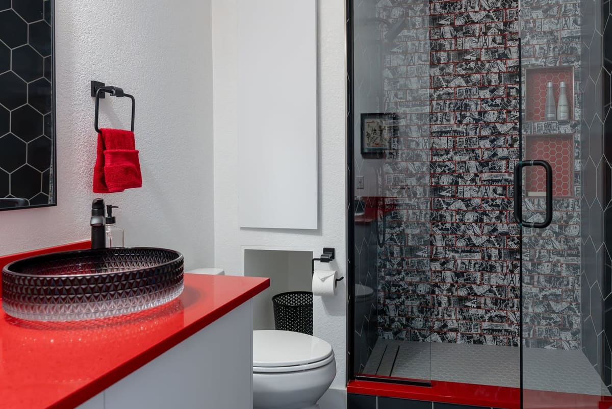 Bathroom with a red quartz vanity, black vessel sink and a graffiti-print subway tile shower with red grout