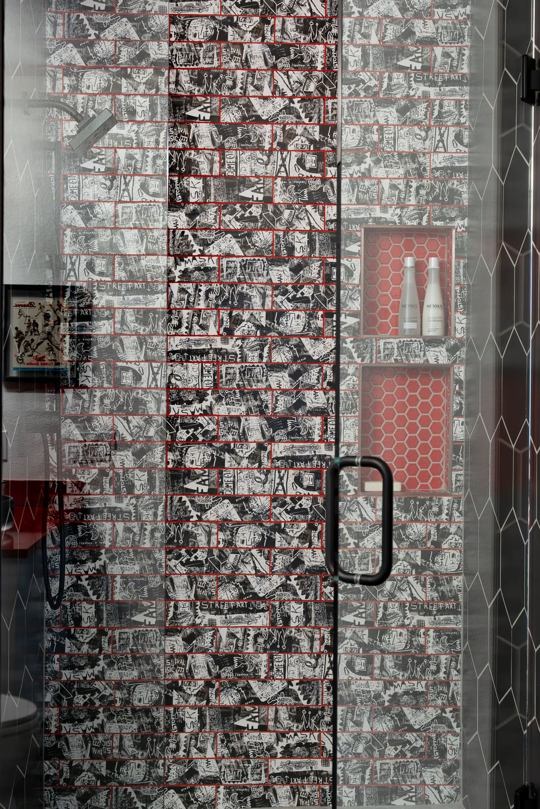 Close view of graffiti-print subway tile with red grout and a red hexagon tile shower niche
