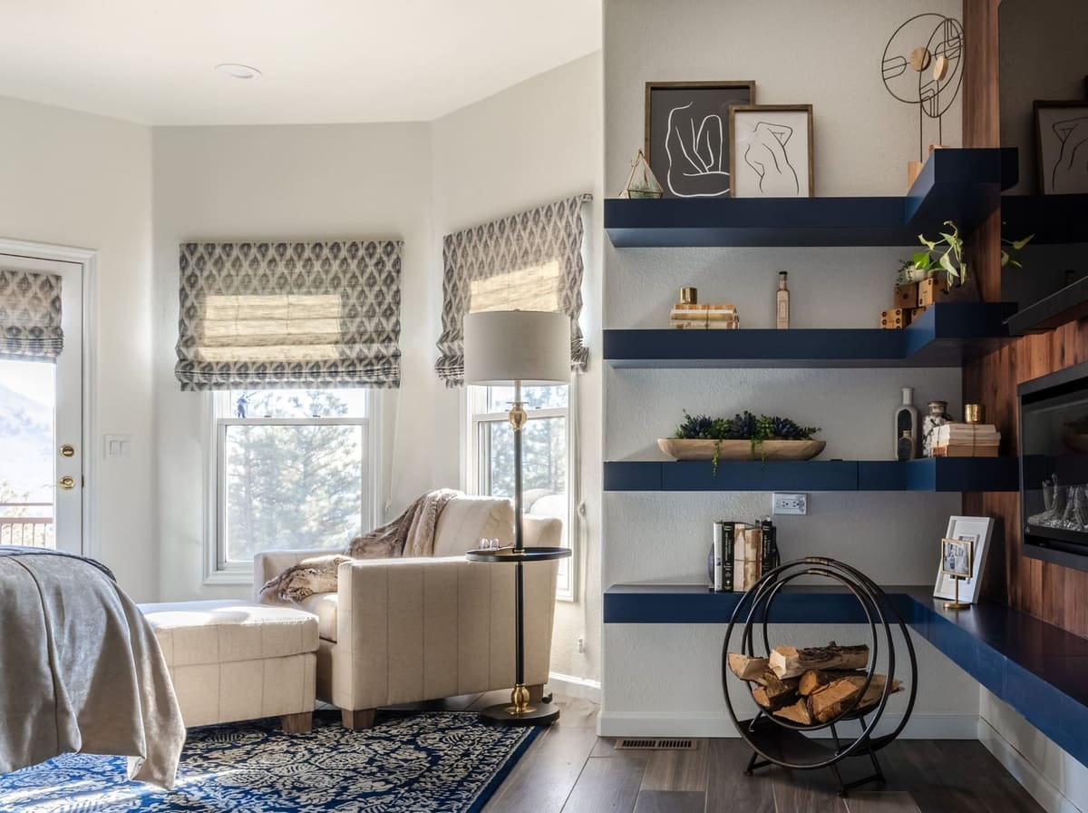 Bay window reading corner with a cream armchair beside navy floating shelves and a log holder