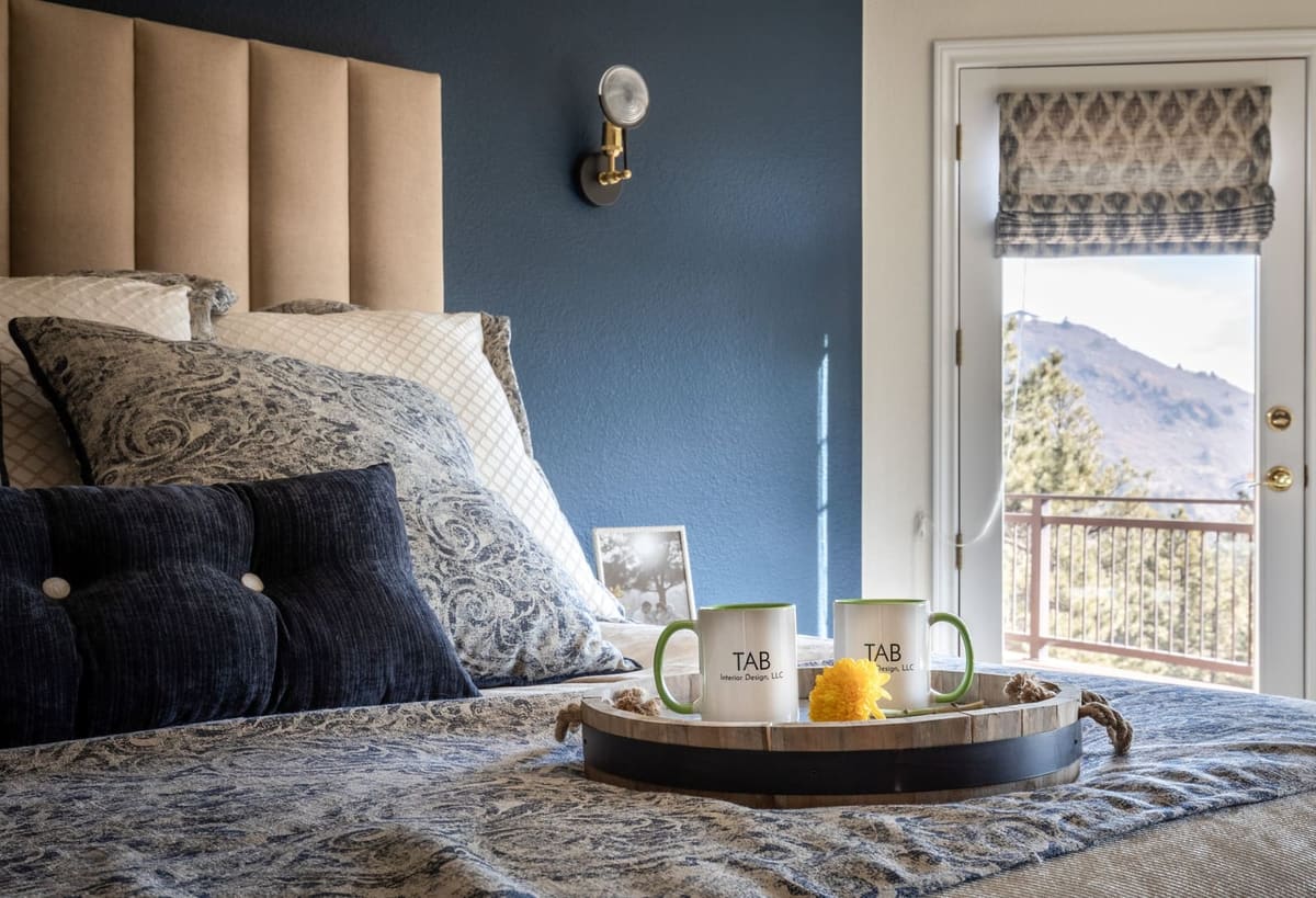 Breakfast tray on the bed beside a navy wall, a balcony door framing the mountains